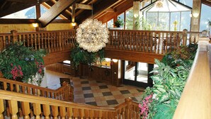 A spacious lobby with wooden railings, a large chandelier, and multiple potted plants.