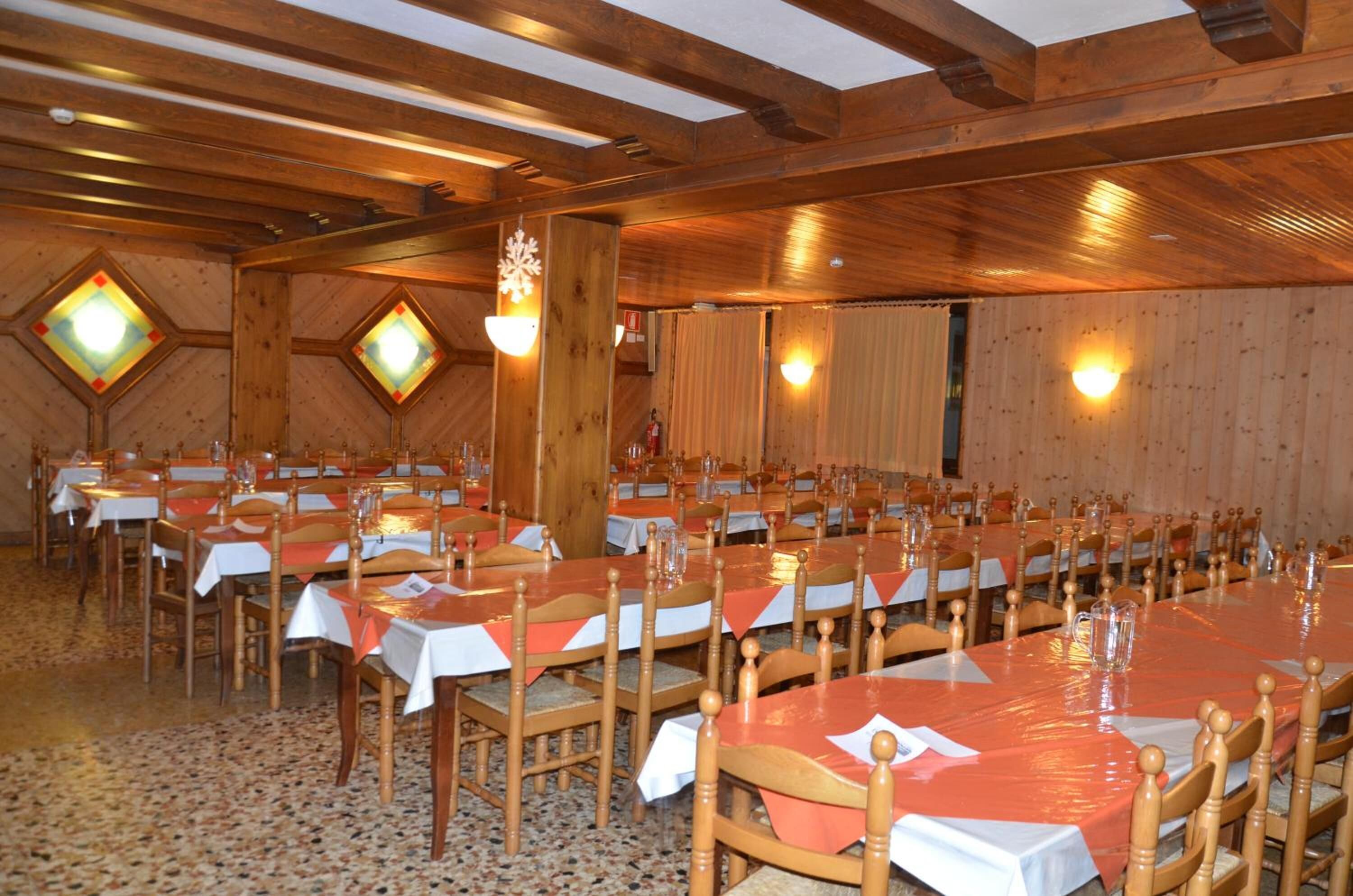 A large hall with multiple tables and chairs, wooden beams on the ceiling, and decorative light fixtures.
