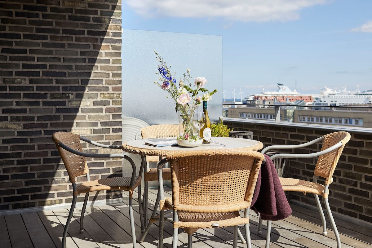 A balcony with wicker furniture, a glass vase with flowers, and a bottle of wine.