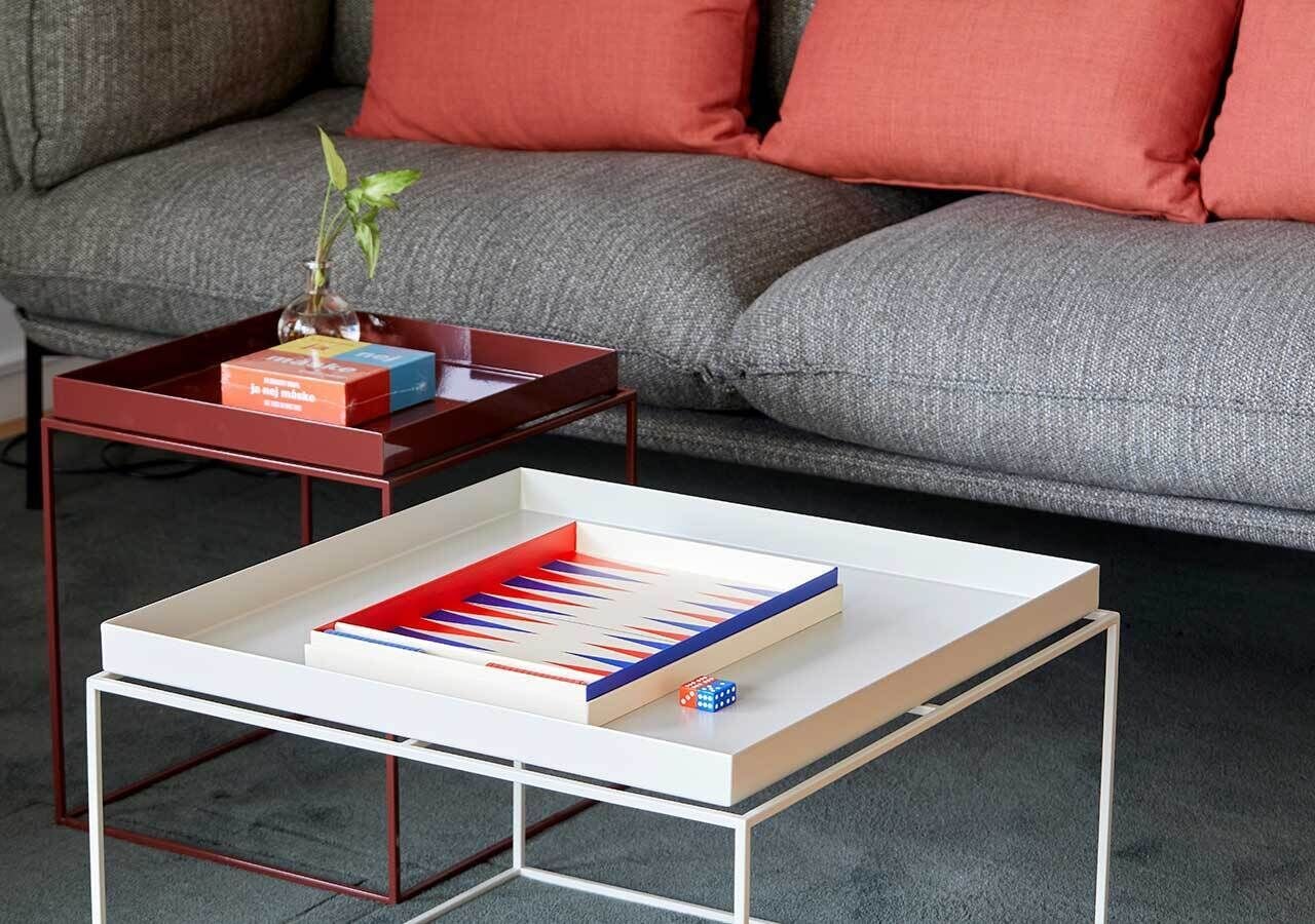 A modern living room with a white coffee table, a red side table with a plant, and a grey sofa with red cushions.