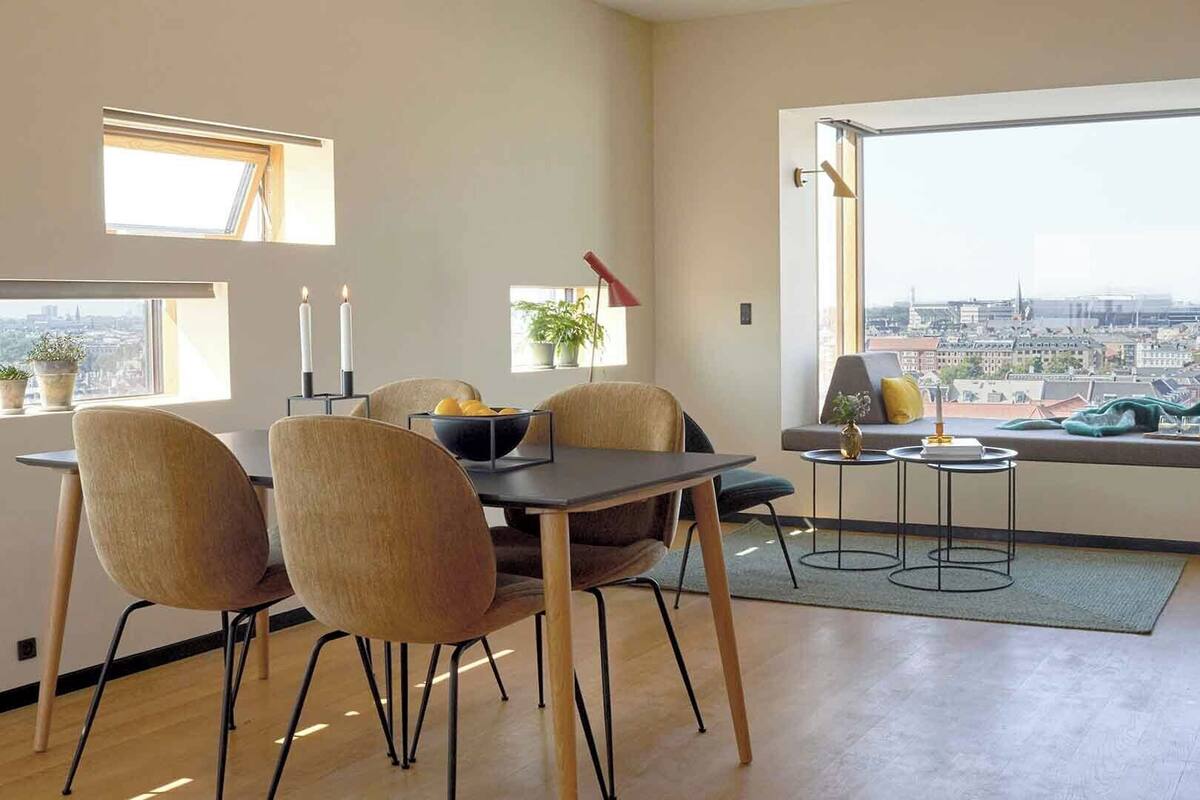 A modern living room with a dining area, large windows with city views, and minimalistic decor.