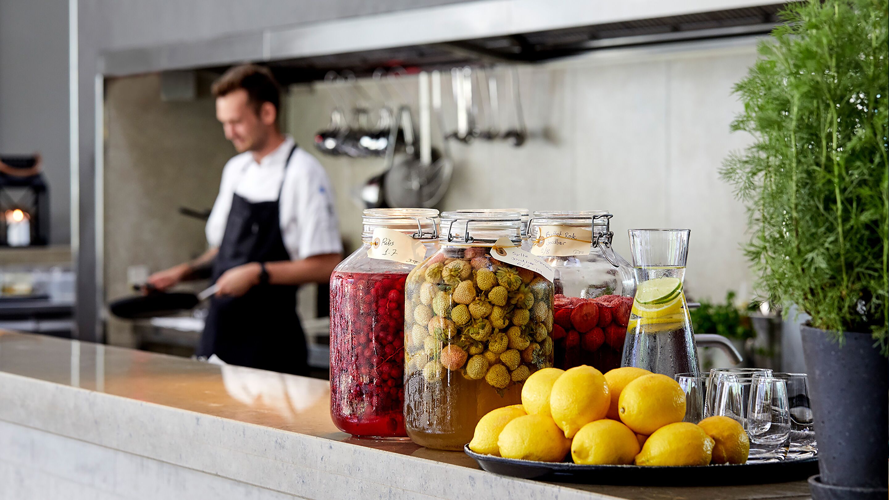 A kitchen counter with jars of preserved fruits and a pitcher of lemonade.
