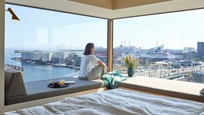 A modern hotel room with a large window overlooking a cityscape, including a harbor and buildings. - Charlottehaven (Copenhagen)