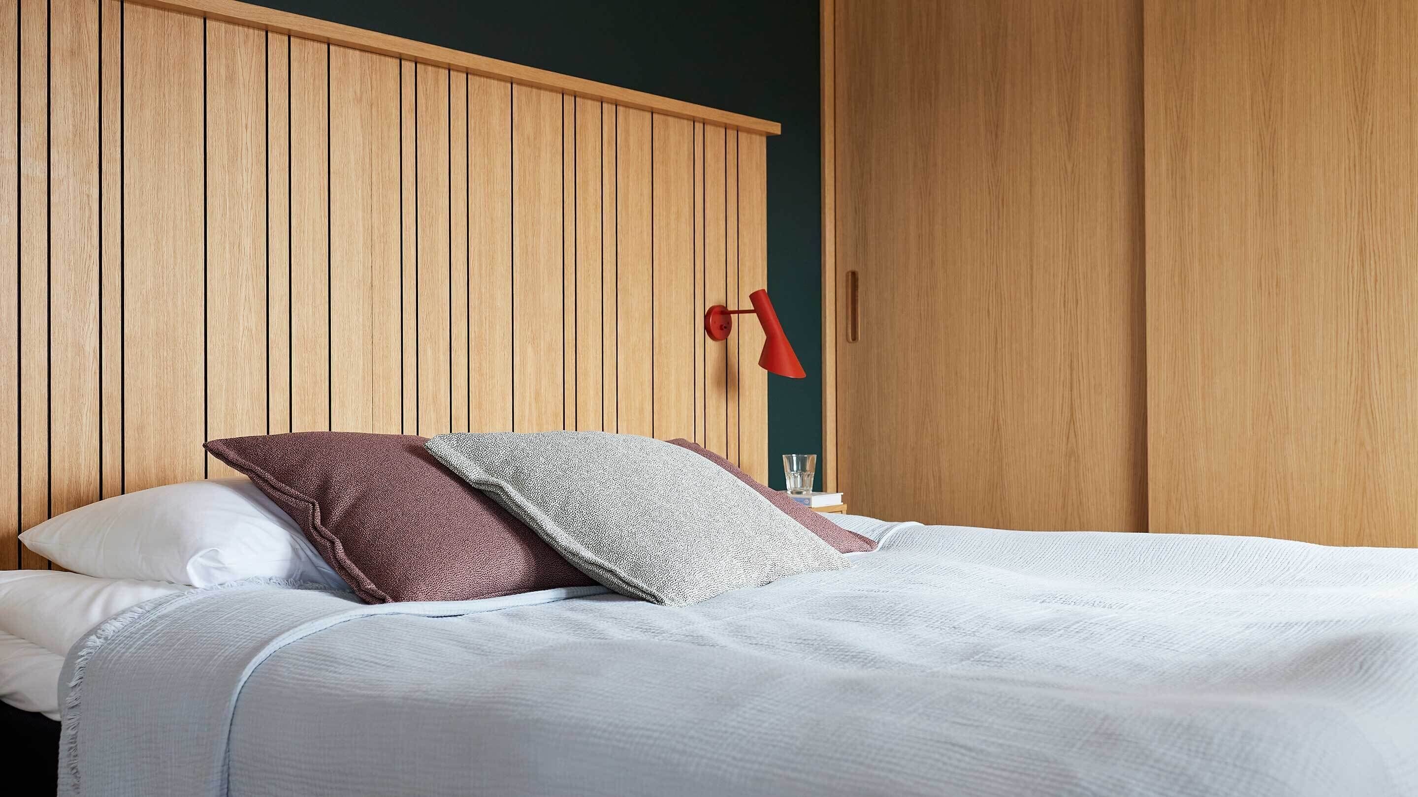 Ein Schlafzimmer mit einem Holzschrank, einem Bett mit weißer Bettwäsche und einer roten Wandlampe.
