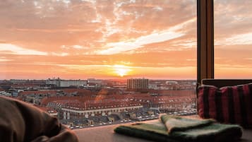 Paisagem urbana ao pôr do sol, com vista pela janela, mostrando uma mistura de edifícios residenciais e comerciais.