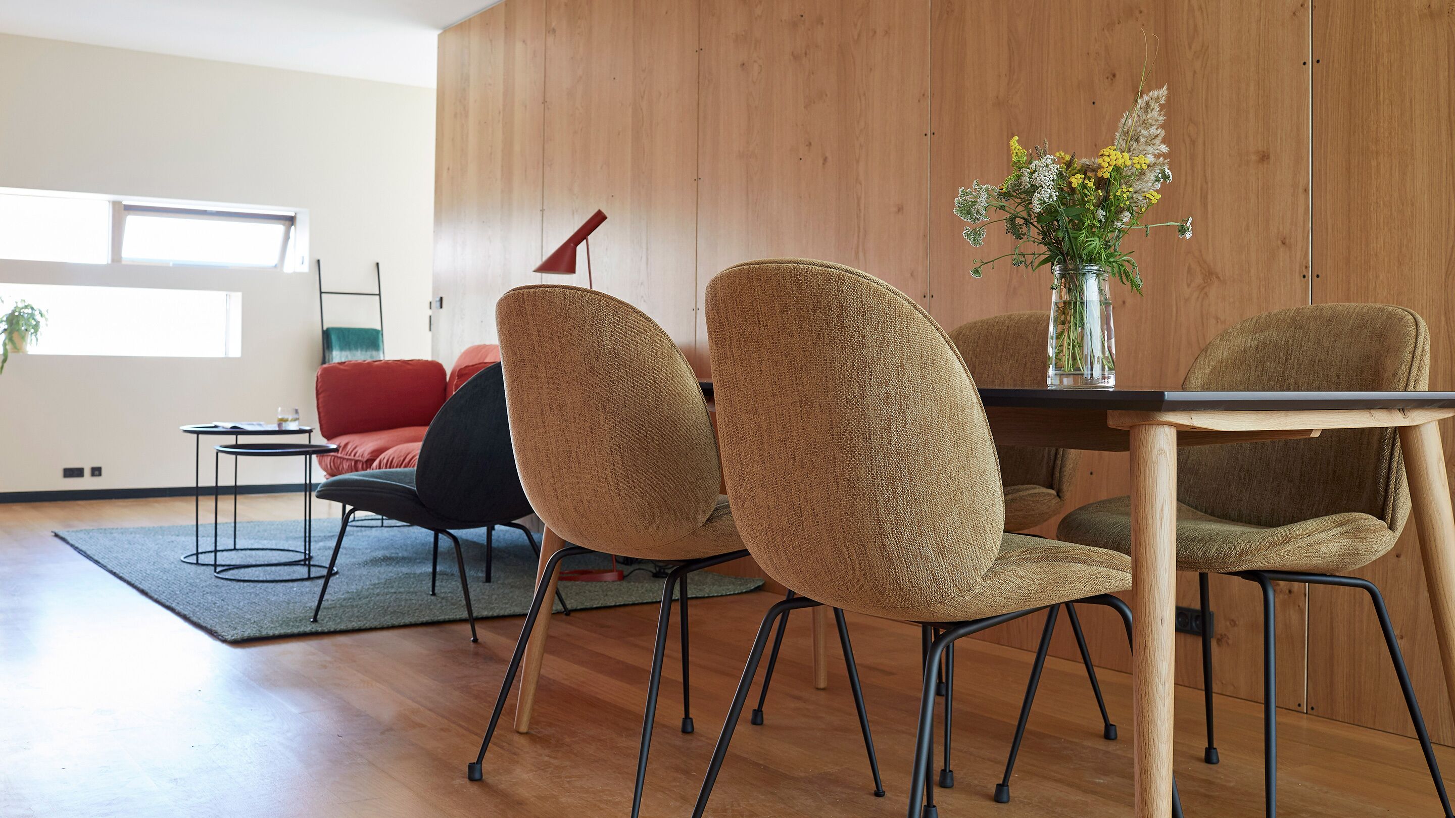 A modern dining area with a wooden table and chairs, a vase with flowers, and a red lamp.