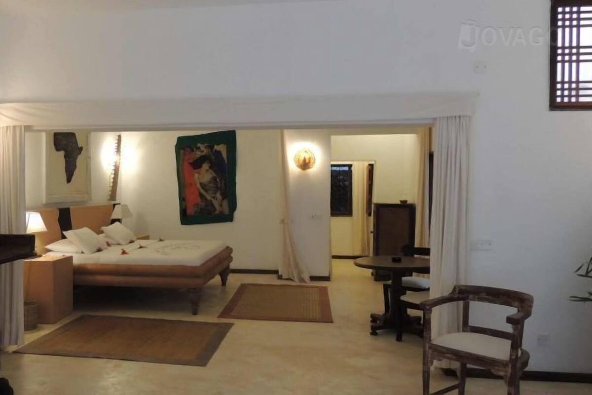 Une chambre d’hôtel comprenant un lit, des tables de chevet, un bureau, une chaise et des œuvres d’art accrochées aux murs.