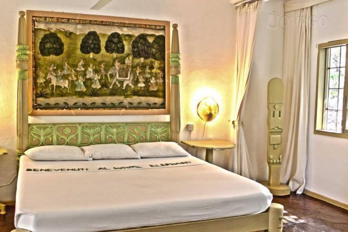 Un lit avec une tête de lit verte, deux lampes de chevet et un tableau accroché au mur au-dessus du lit.