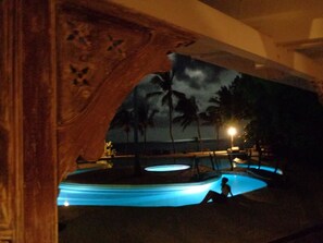 A nighttime view of a pool area with a person sitting by the pool, palm trees, and a night sky. - White Elephant Sea & Art Lodge (Malindi)
