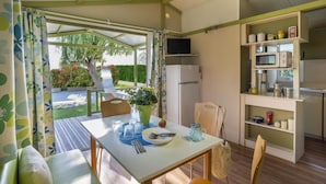 Una habitación compacta y bien iluminada con una mesa de comedor preparada para dos personas, una pequeña kitchenette y un televisor montado en la pared.