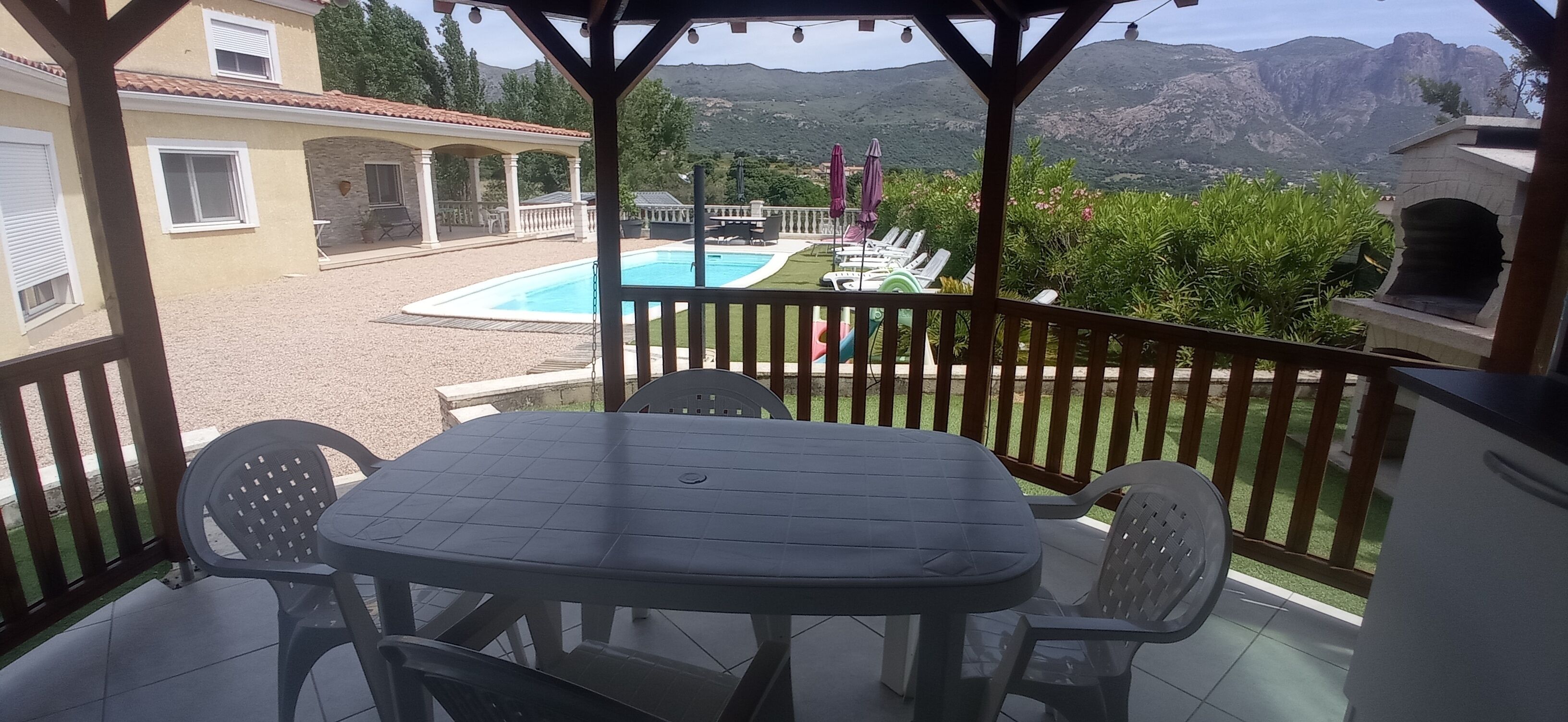 Ein überdachter Außenbereich mit Pool, Stühlen und einem Tisch.