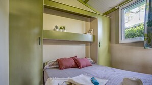 Un dormitorio con cama, almohadas, un sombrero y una ventana con vistas a follaje.