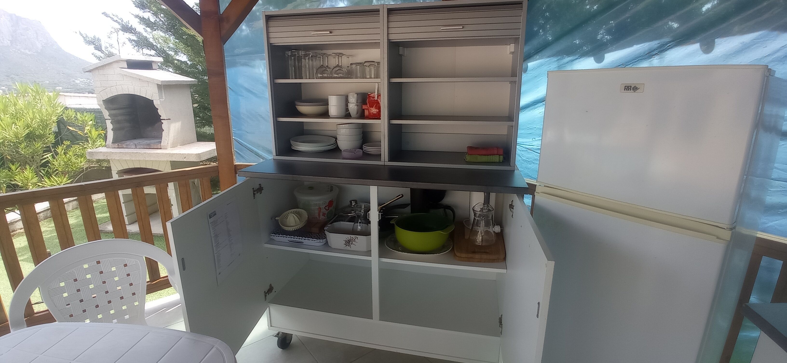 A kitchen area with a built-in shelf unit containing various kitchenware, a refrigerator, and a stone oven.