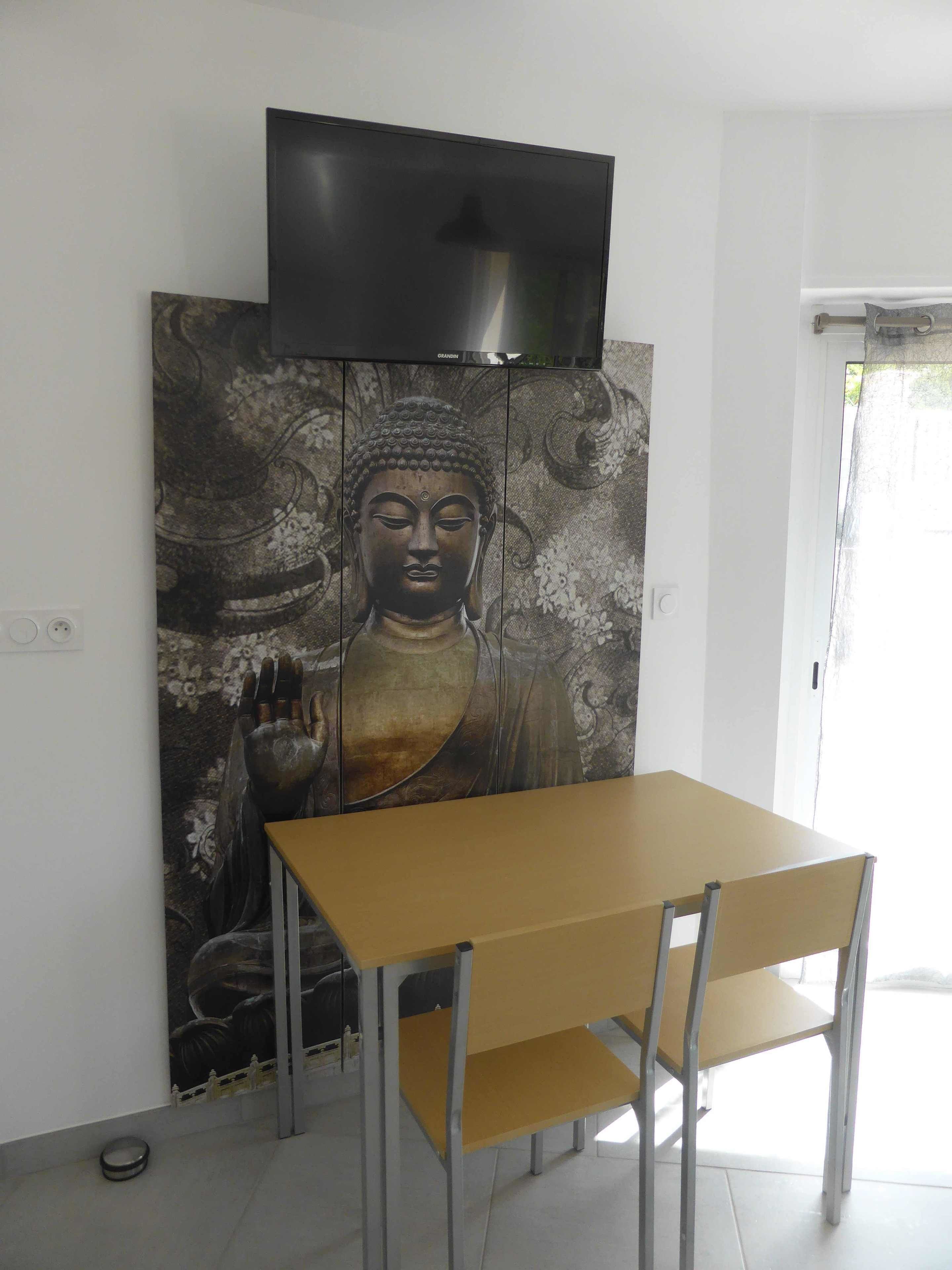 Ein Essbereich mit Tisch und Stühlen, einem Buddha-Gemälde und einem flachbildfernseher, der über dem Gemälde angebracht ist.