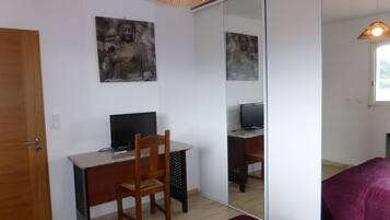 Un dormitorio con cama, escritorio con computadora, silla, armario y un espejo grande.