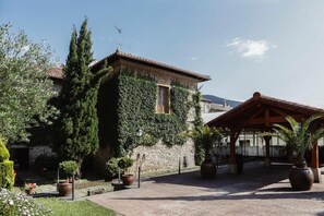 A courtyard with a stone building covered in ivy, potted plants, and a wooden pergola. - Hotel Convento San Roque (Balmaseda)