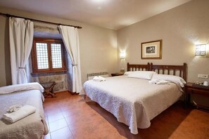 A bedroom with a large bed, a smaller bed, a window with curtains, a radiator, a nightstand, and a framed picture on the wall. - Hotel Convento San Roque (Balmaseda)