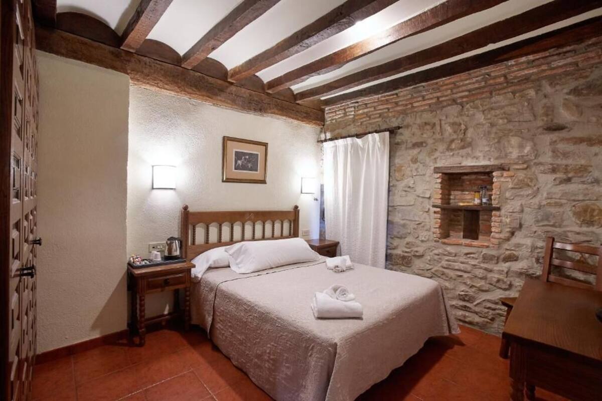 A cozy room with a stone wall, a wooden bed, a nightstand, and a small table.