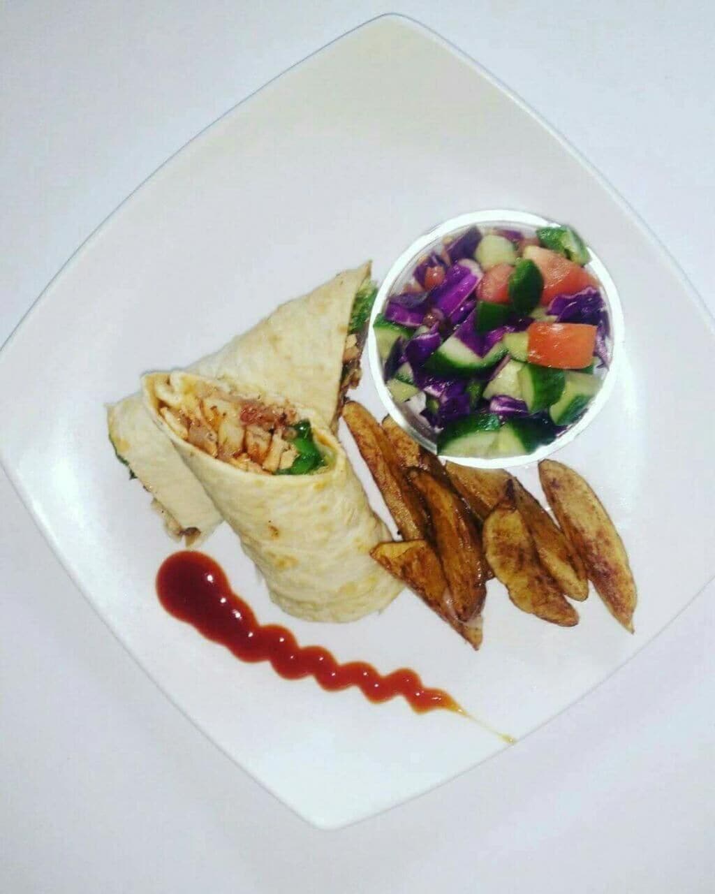 A plate with a wrap, a side salad, and roasted potatoes.