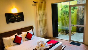 A hotel room with a bed, a painting on the wall, a sliding glass door to a garden, and a view of trees and rocks. - Hantara Udawalawa (Udawalawa)