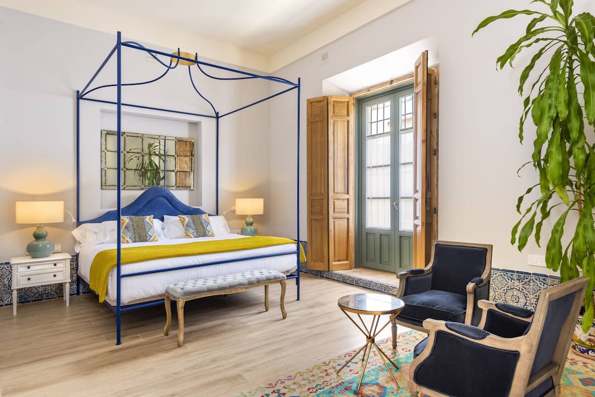 Camera da letto con un letto a baldacchino, una porta in legno, una pianta grande e due poltrone.