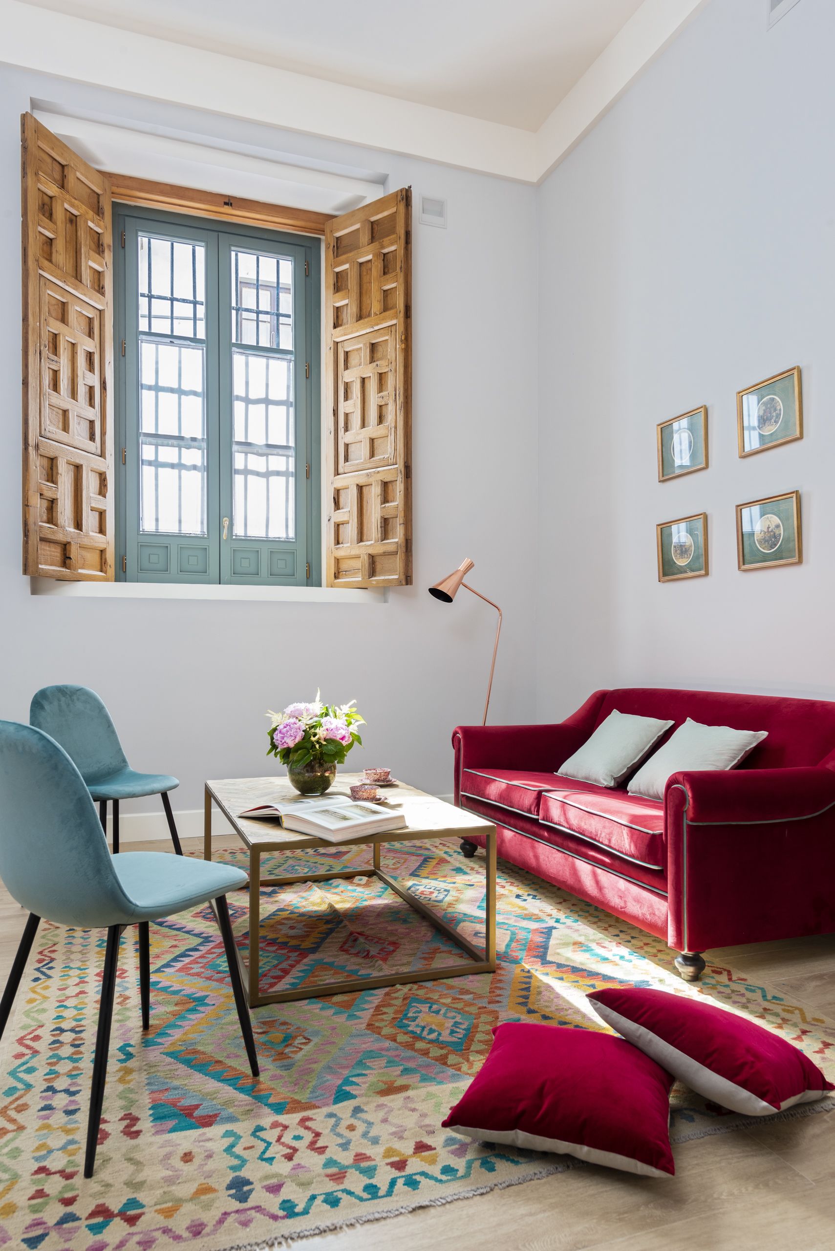 A room with a red sofa, a blue chair, a coffee table with a vase, and a colorful rug.
