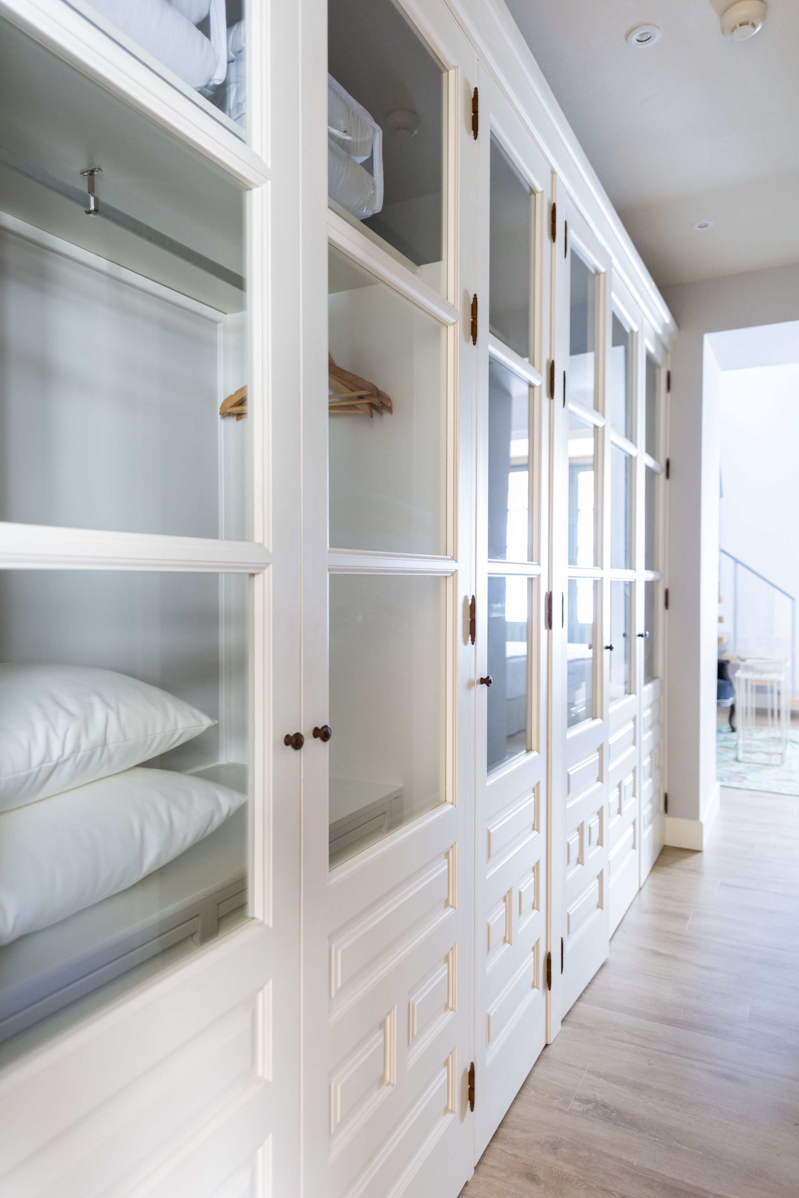 Un dressing spacieux, doté de nombreuses étagères et de tiroirs, avec un parquet en bois clair et une vue sur un escalier en arrière-plan.