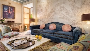 A living room with a blue sofa, patterned armchairs, a coffee table with magazines, and a painting on the wall. - Palacio Bucarelli (Seville)