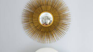Una cama con ropa de cama blanca y almohadas rojas, un cabecero blanco y un espejo grande con motivos de sol dorados y blancos en la pared.