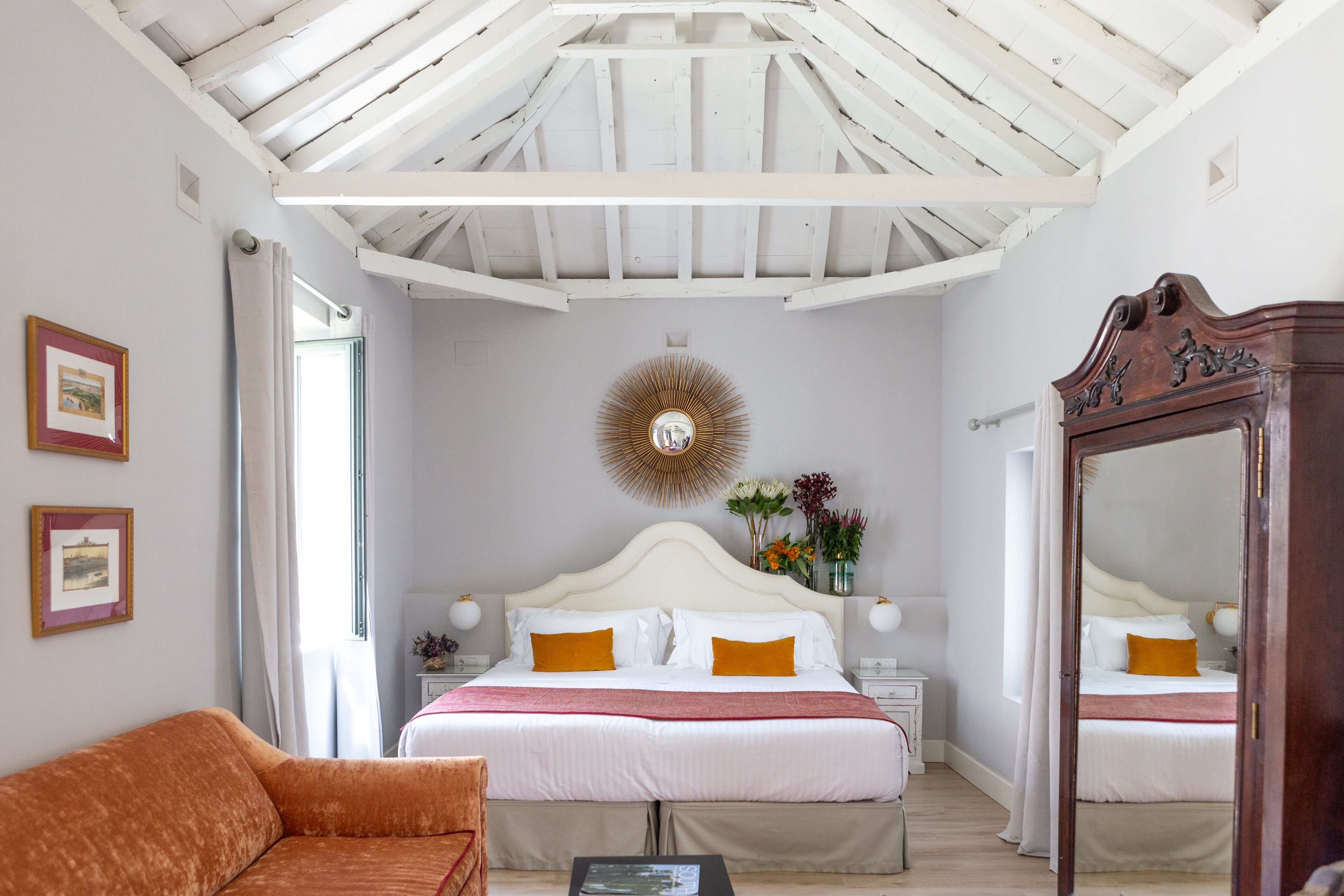 A bedroom with a large bed, a wooden wardrobe, a sofa, and a mirror.