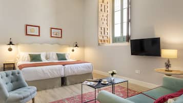 Un dormitorio con cama, mesitas de noche, televisor y una zona de estar con sofá y sillón.