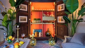 A cozy corner with a wooden shelf displaying various items, surrounded by large green plants. - Palacio Bucarelli (Seville)