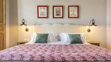 A neatly made bed with a patterned bedspread, two wall-mounted lamps, and three framed pictures on the wall.