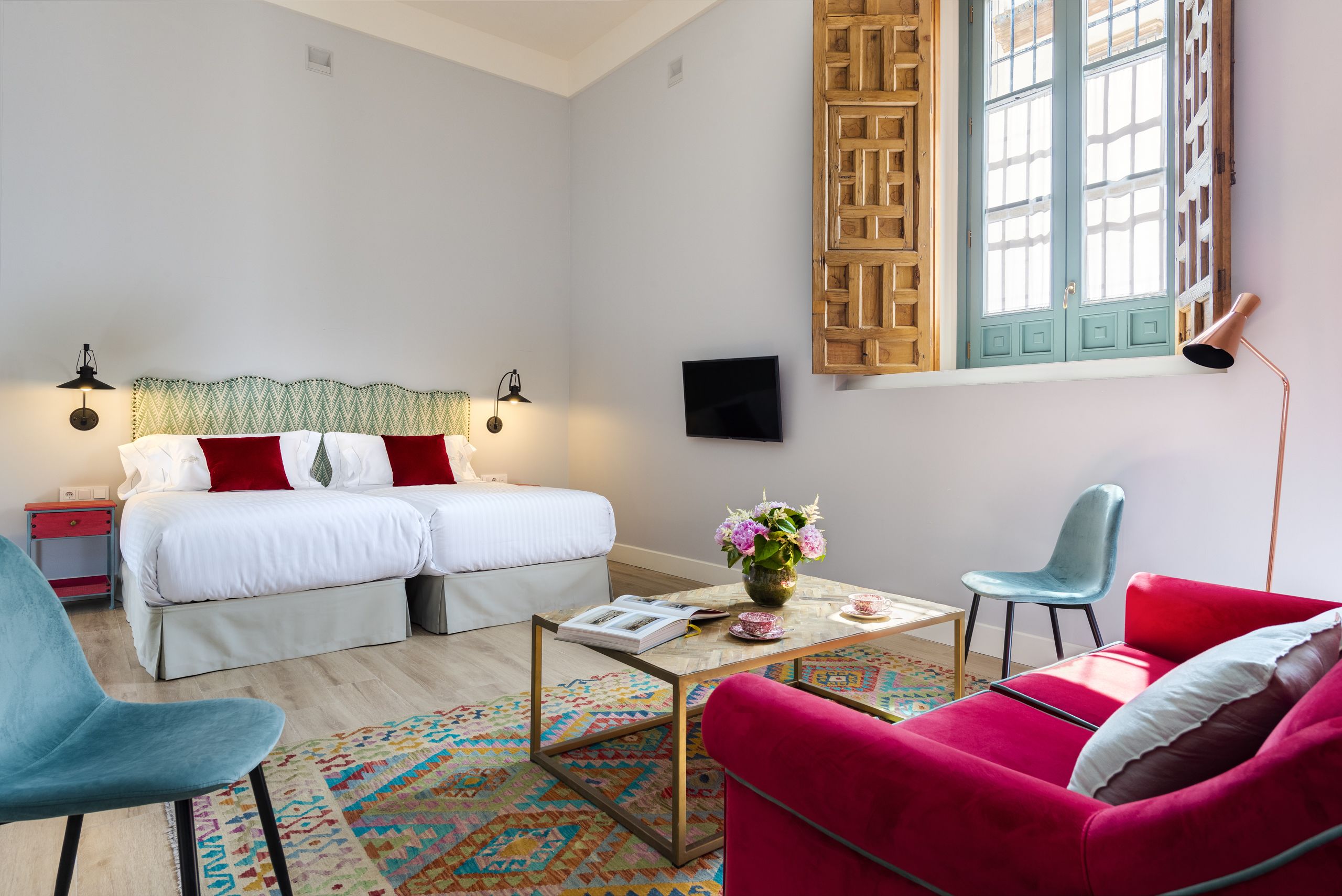 A bedroom with a bed, two bedside tables, a TV, a coffee table with a vase, a chair, and a couch.