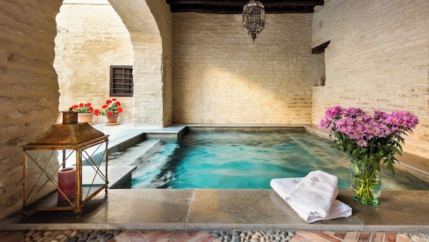 A spa area with a stone pool, a lantern, and a vase of flowers. - Palacio Bucarelli (Seville)