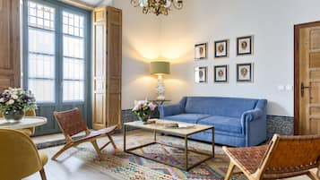 A living room with a blue sofa, wooden chairs, a coffee table, and a patterned rug.