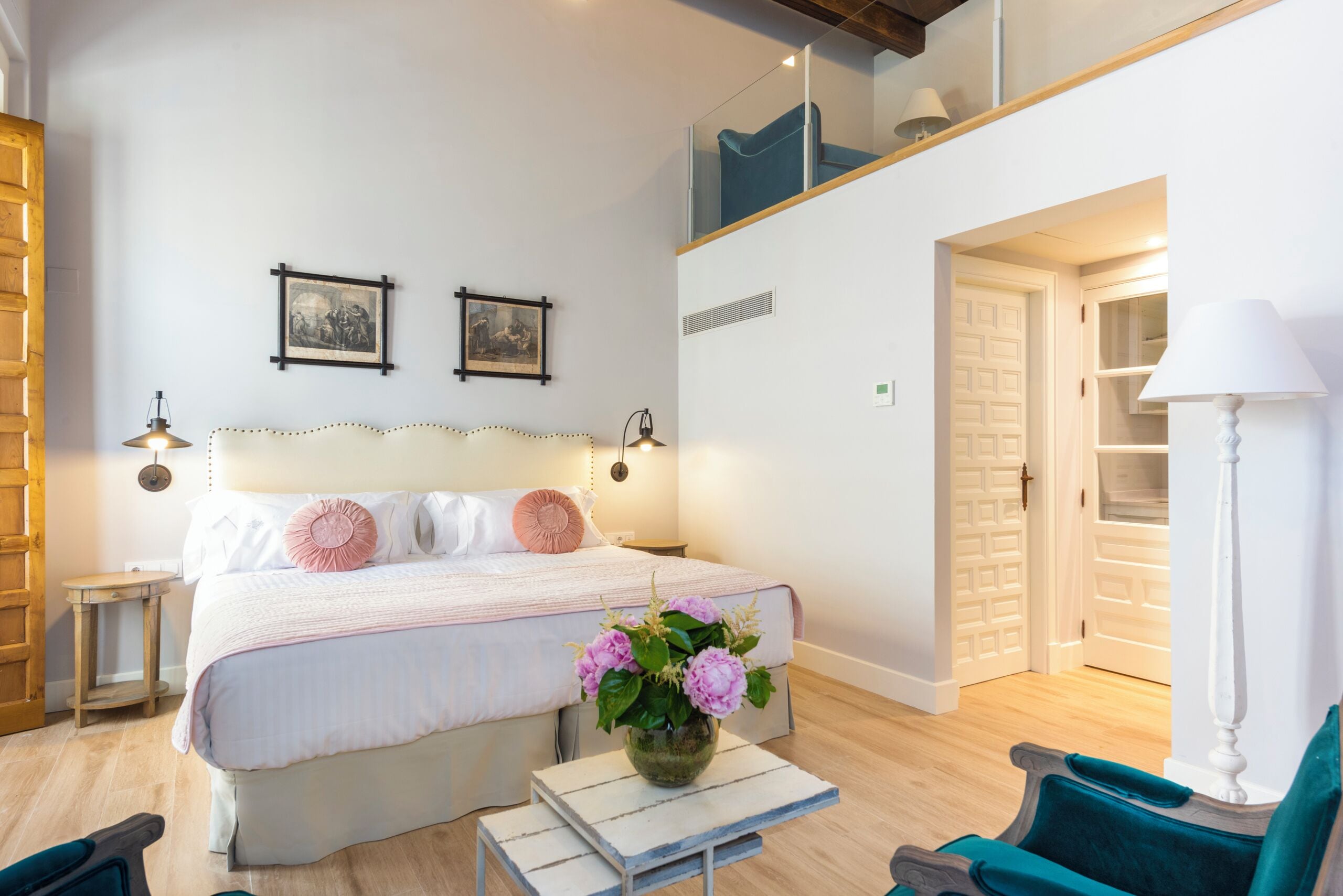 Une chambre à coucher avec un lit, des tables de chevet, un vase avec des fleurs, une chaise et un escalier.
