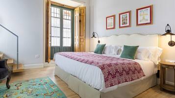 A bedroom with a large bed, a wooden door, a staircase, and a small table with a lamp.