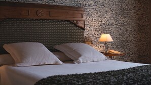 A hotel room with a bed, pillows, a wooden headboard, a patterned wall, a lamp, and a telephone. - Hotel Konbenio (Amorebieta)