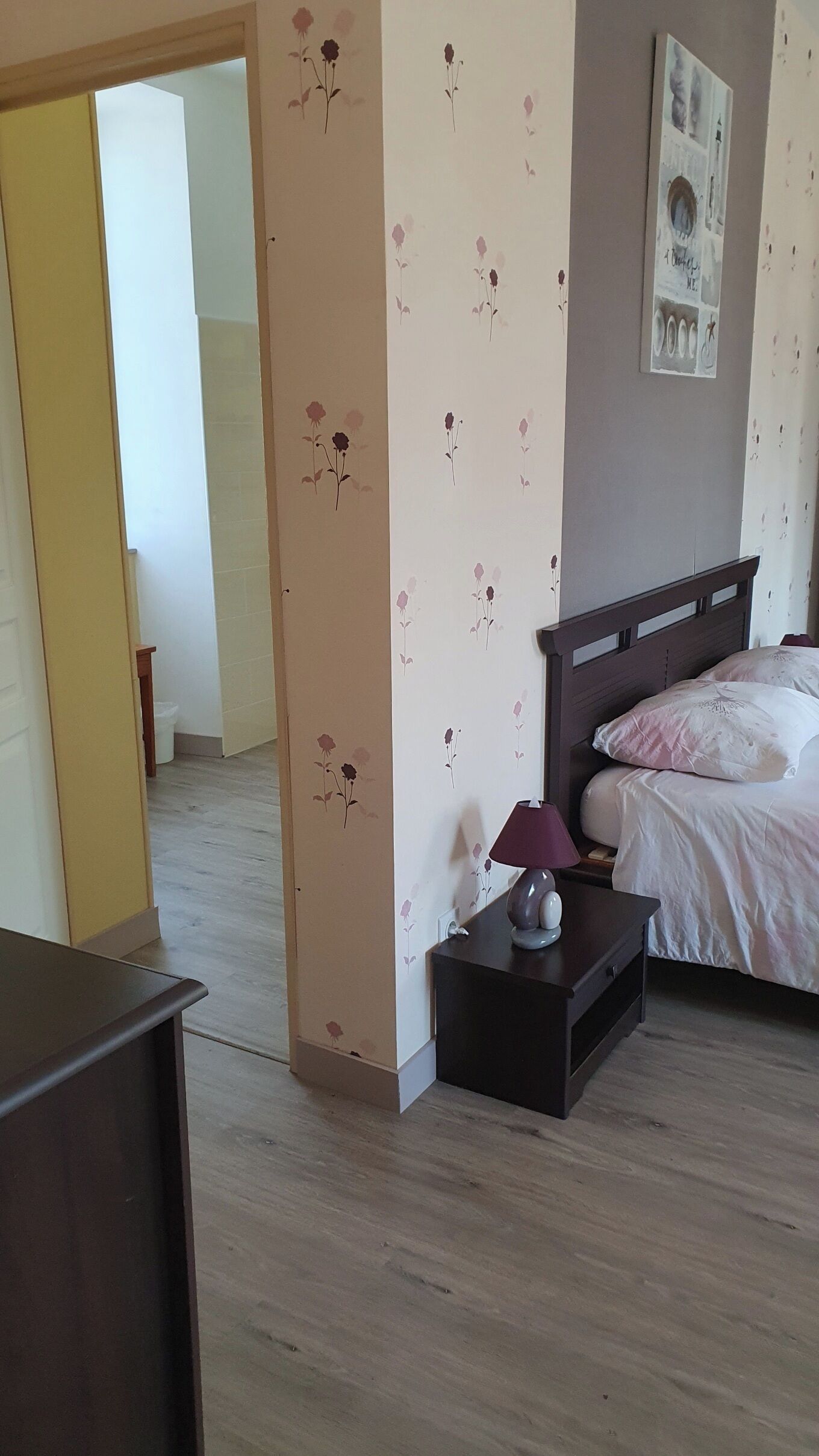 A bedroom with a bed, bedside table, lamp, and a wall with floral wallpaper.