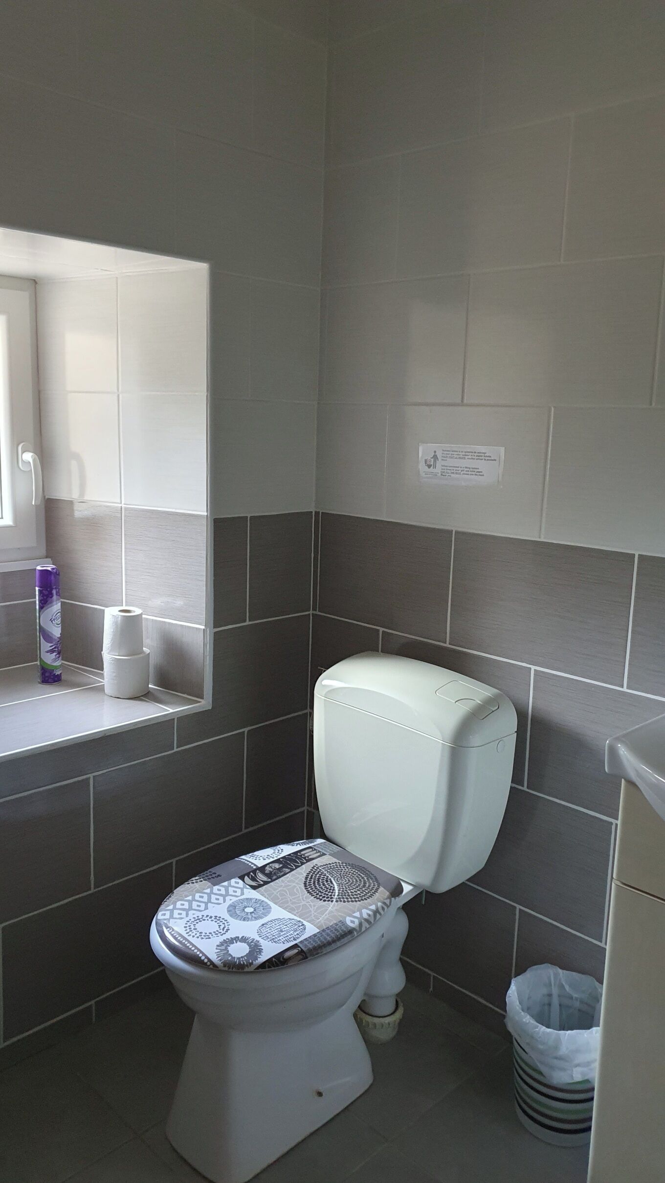 Un baño con un inodoro, un cubo de basura y un rollo de papel higiénico en un estante.