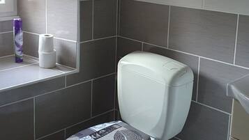 Un baño con un inodoro, un cubo de basura y un rollo de papel higiénico en un estante.