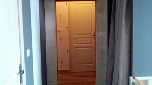 Un pasillo estrecho con una puerta cerrada al final, un interruptor de luz en la pared y un radiador a la derecha.