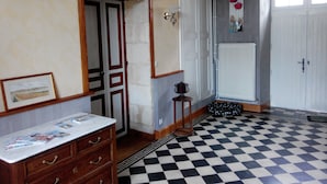 Una habitación con piso a cuadros, un aparador de madera con cajones, una puerta con marco blanco y un radiador en la pared.