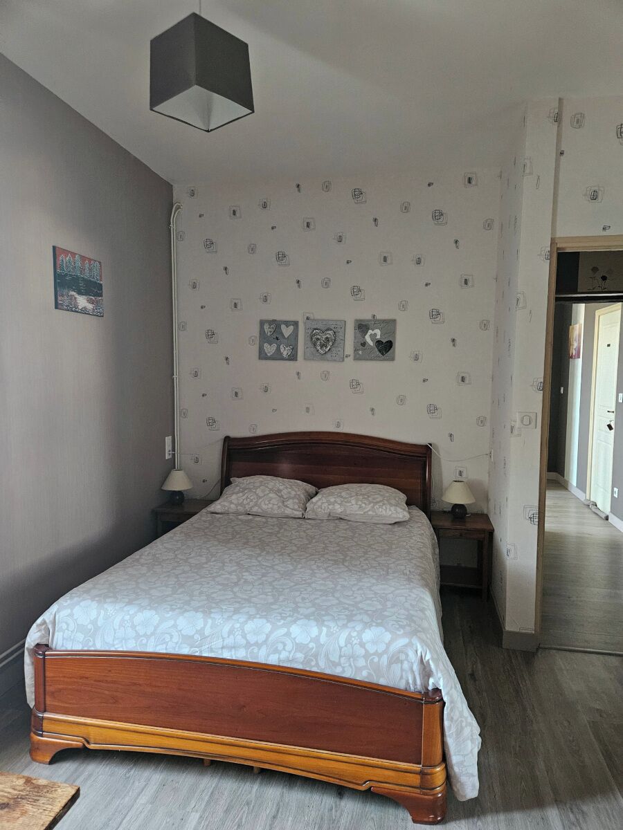 A bedroom with a wooden bed, a nightstand, a lamp, and a wall with heart-patterned decorations.
