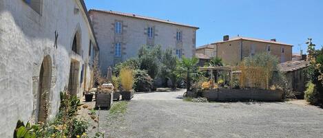 A courtyard with a gravel path, a building with arched windows, and a clear blue sky.