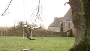 A grassy backyard with a swing set, a large tree, and a stone wall. - Le Manoir de la Baronnie (Boischampré)