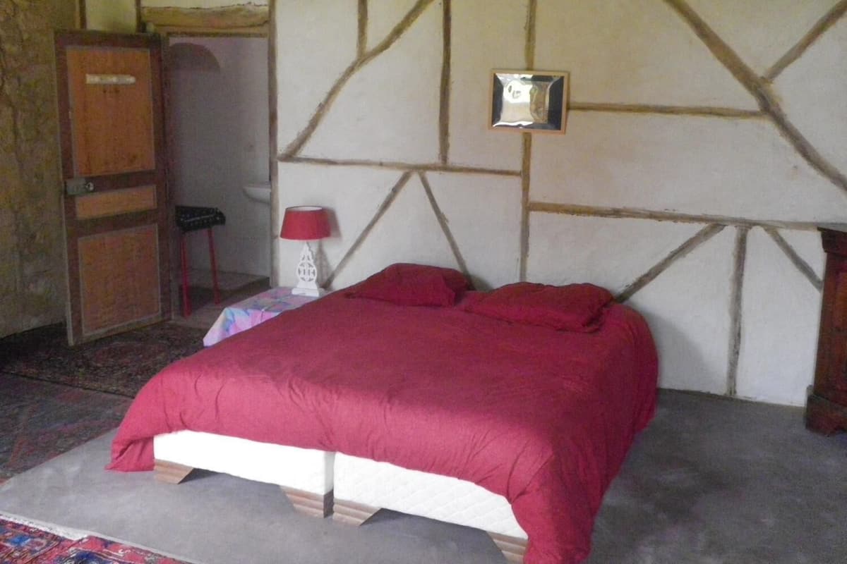 A bed with a red bedspread in a room with a stone wall and a wooden door.