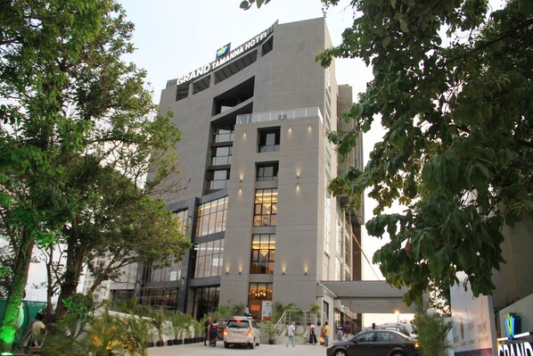 A modern hotel building with a prominent sign, large windows, and a parking area. - Grand Tamanna Hotel Hinjawadi Pune (Paud)