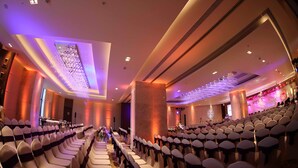 Un salón de conferencias con filas de sillas, un escenario e iluminación en el techo.